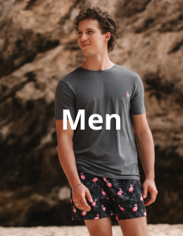 Man walking on the beach wearing a flamingo‑pattern t‑shirt and swim shorts set from the brand Hamabe. 
